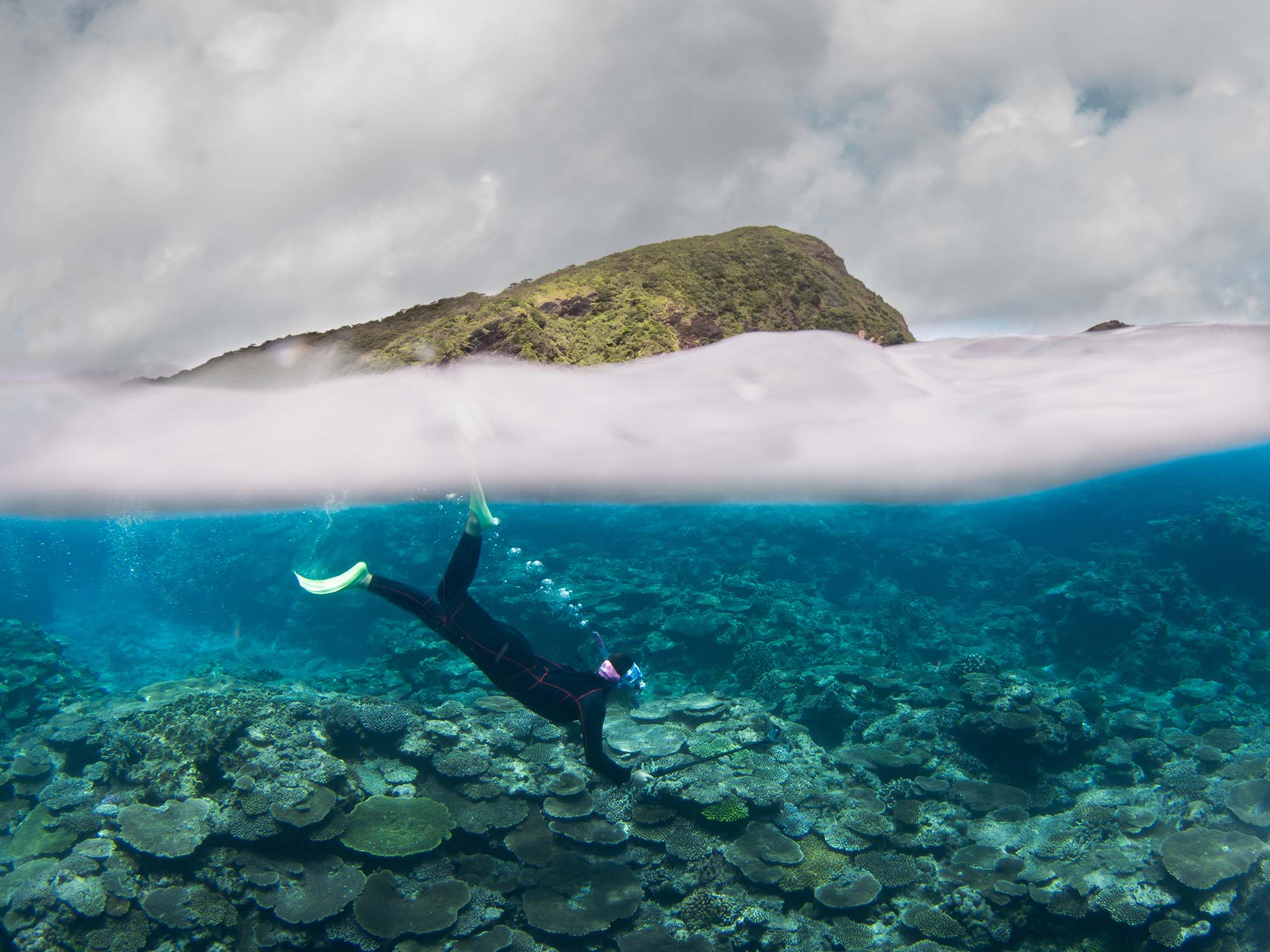 Ikelite Featured Customer Michael Corso shooting with Sony Alpha Camera inside an Ikelite Underwater Housing, split shot with coral reef underwater and mountain with clouds in background